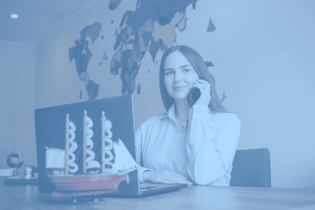 A woman sits at a desk with a laptop and a model ship, discussing maritime accounting services on the phone. A world map is displayed on the wall behind her. The image has a blue tint.