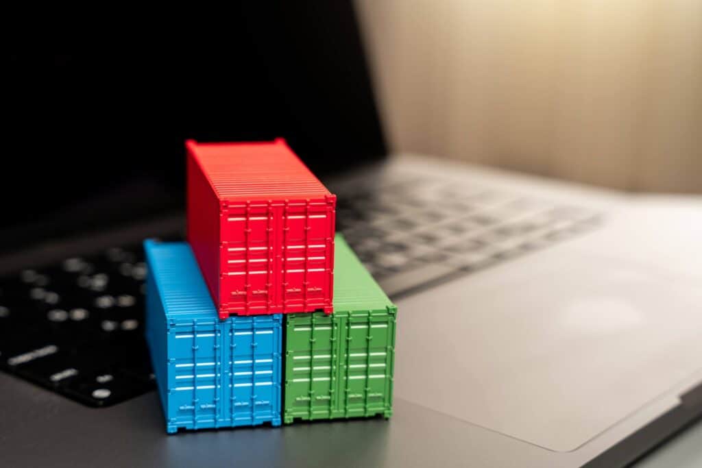 Three small model shipping containers—red, blue, and green—stacked on a laptop keyboard, symbolizing how freight forwarders and logistics service providers leverage technology for digital containerization.