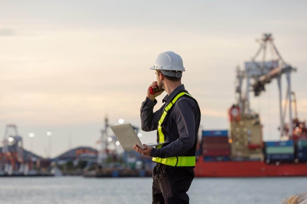 A vessel agent looking at a cargo ship during a port call planning checklist