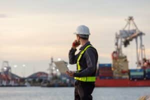 A vessel agent looking at a cargo ship during a port call planning checklist
