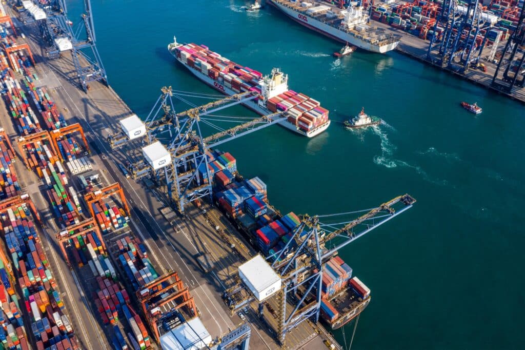 An arial view of a busy port with a cargo ship coming in with tugs.