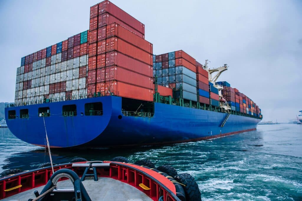 Tugboat assisting a large container ship during port call changes near a busy harbor