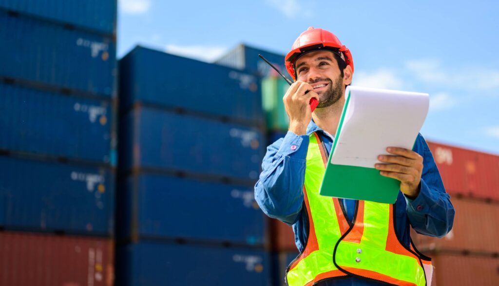 A vessel agent on a walkie talkie with a clip board discussing a port call report.