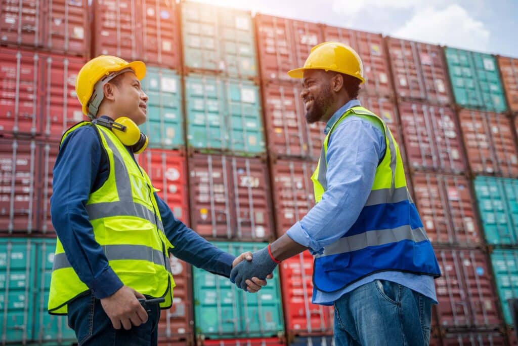 Two port operators shaking hands in front of containers, representing agreements and coordination tied to port tariffs