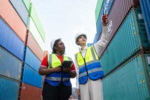 Port workers reviewing container stacks and coordinating operations related to port tariffs in a busy shipping yard