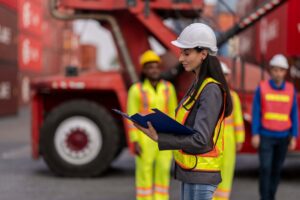 Port worker checking documents during the shipping documentation process with crew and equipment in background