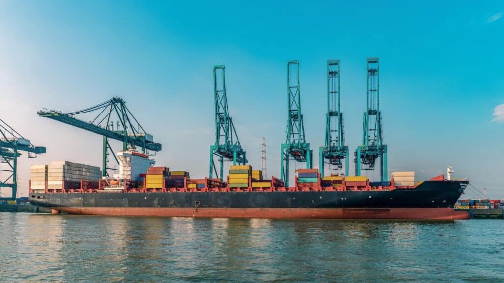 Port agent vs ship agent comparison with a container ship docked beside harbor cranes at a busy port