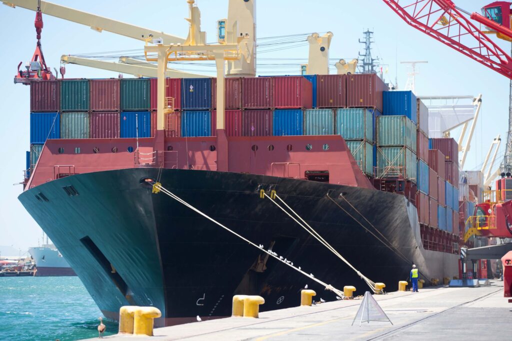 Port agent vs ship agent roles illustrated by a cargo ship moored at a dockyard with containers on deck