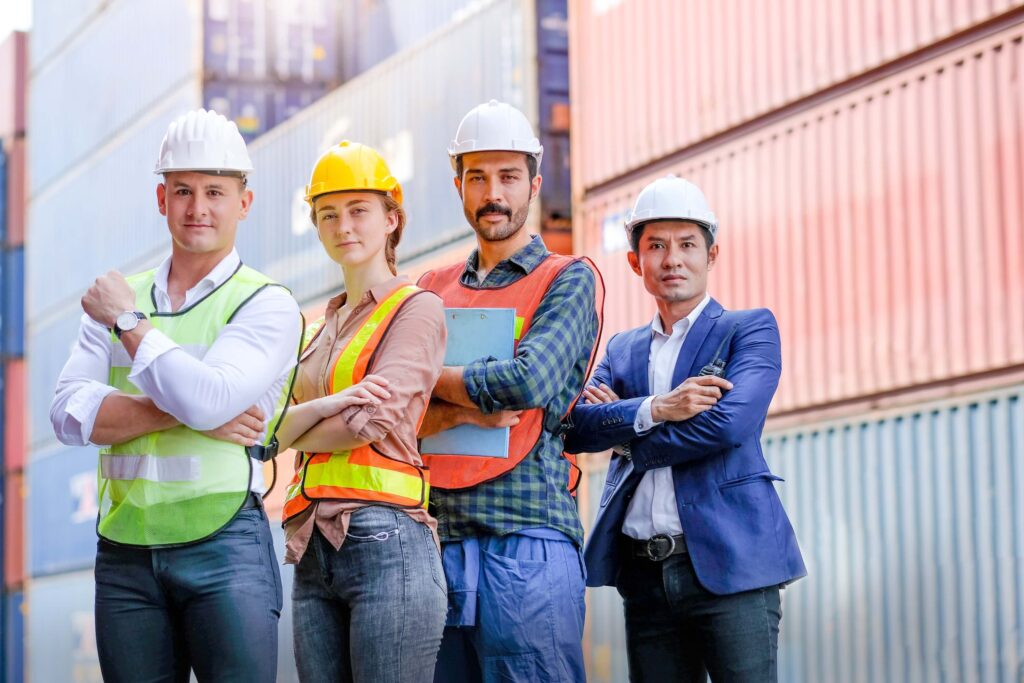 Port agent vs ship agent team standing in hard hats and safety vests among stacked shipping containers