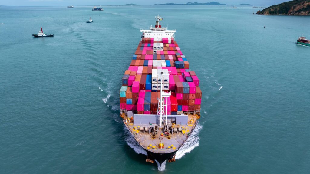 Container ship underway with tug support, representing voyage management system vs port call software from voyage tracking to port-call coordination.
