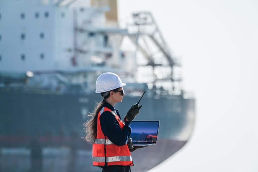 Port agent performance monitoring by a logistics professional using a radio and laptop near a vessel