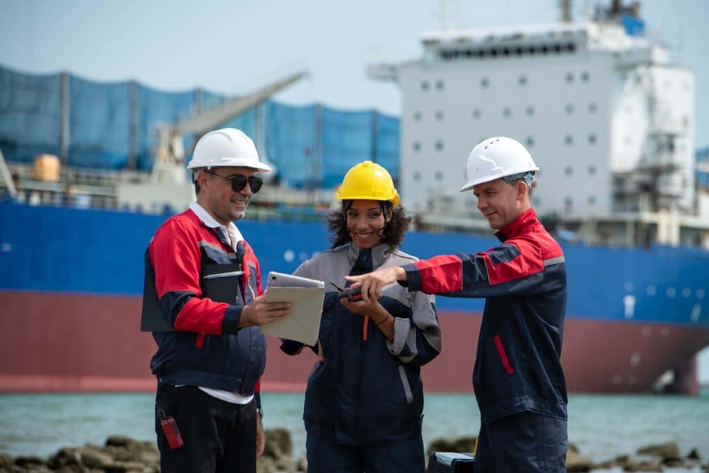 Port operations team reviewing vessel activity and outsourced disbursement account processing near a cargo ship